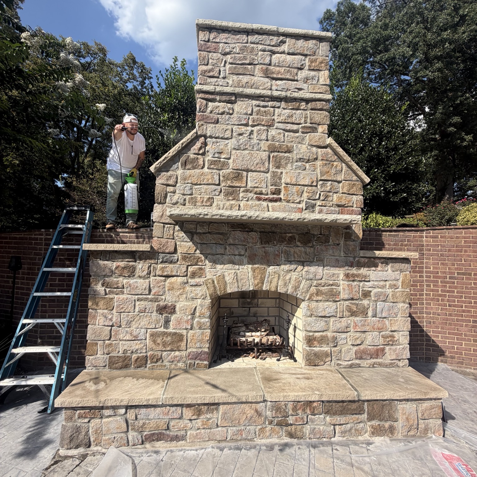 Outdoor stone fireplace with arched firebox, mantel, and hearth during final cleaning